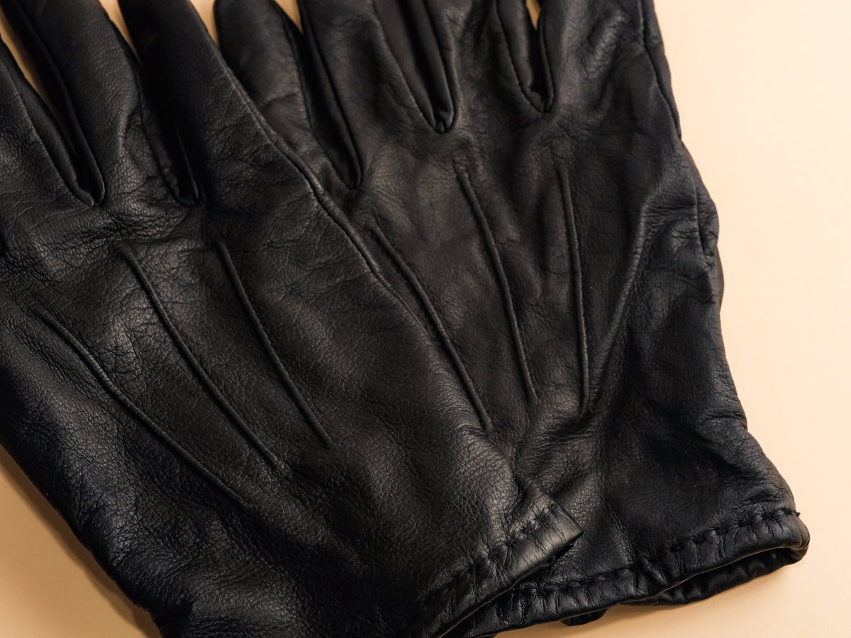 Close-up of soft black leather gloves on a tan background